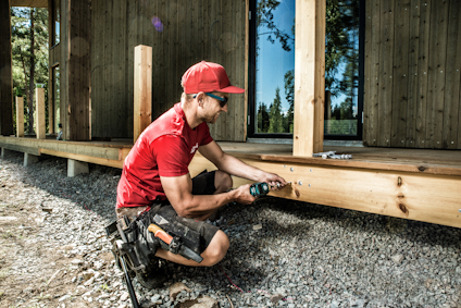 En person använder en skruvdragare för att fästa en bärlina vid ett altanbygge utomhus.