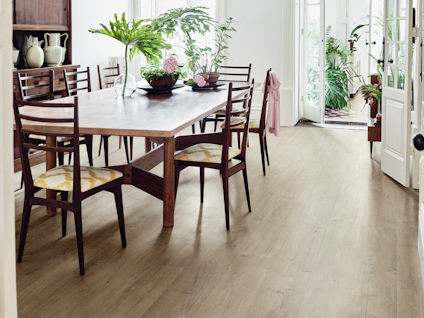 Matbord med mörka trästolar, gröna växter på bordet. Trägolv och växter vid öppnad dörr.