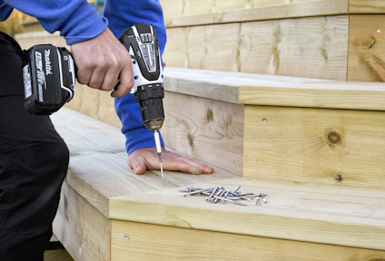 Person som använder en sladdlös borr på en trätrappa med skruvar bredvid.