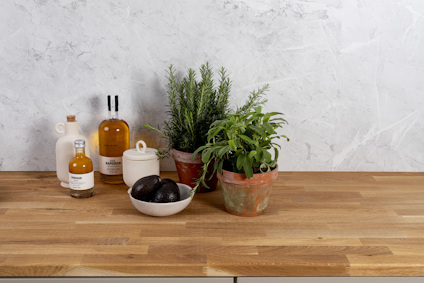 Kryddväxter i terrakottakrukor, avokado i en skål, och flaskor på en träbänkskiva mot en ljus stenvägg.