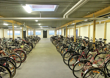 Cykelrum med flera cyklar parkerade i rader under ett tak med takfönster.
