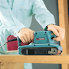 Person använder en blå Makita bandslipmaskin på ett trästycke.