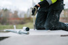 Kneeling worker with high-visibility jacket using a wire brush on concrete, with tools in the background.