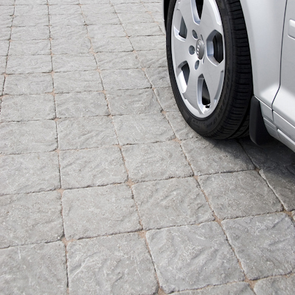 Engrår stenbeläggning med mönster bredvid ett bilhjul.