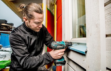 En person skruvar fast fönsterbleckplåt vid ett fönster med fönsterbleckskruv.