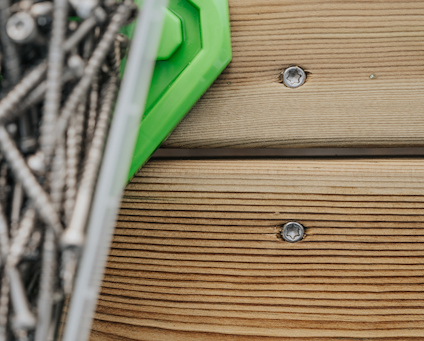 Monterad trallskruv sedd uppifrån, fastskruvad i trallbräda. Till vänster syns delar av förpackningen med fler trallskruvar.