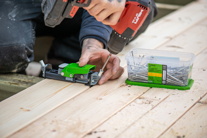 En person placerar en skruv i ett trallmonteringsverktyg för dolt montage och förbereder att skruva fast skruven i en trallbräda med en skruvdragare.