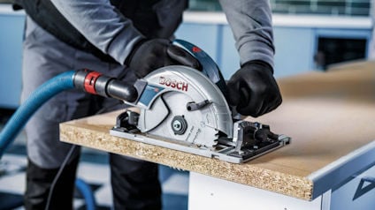 Person med skyddshandskar använder en Bosch cirkelsåg för att såga en träskiva.